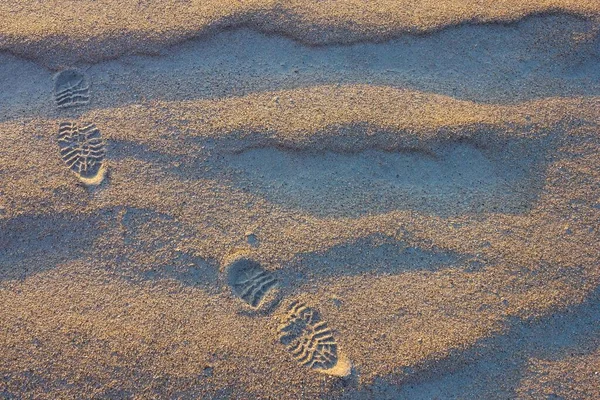 Sand, natural texture. Relief tracks from shoes. Road, path, walking route. View from above. Lateral solar lighting.