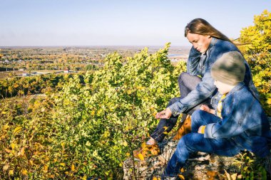 Doğada genç bir anne ve oğul. Modern kot elbiseler, gündelik tarz. Uzakta ufuk çizgisi, mavi gökyüzü. Yanal güneş ışığı.