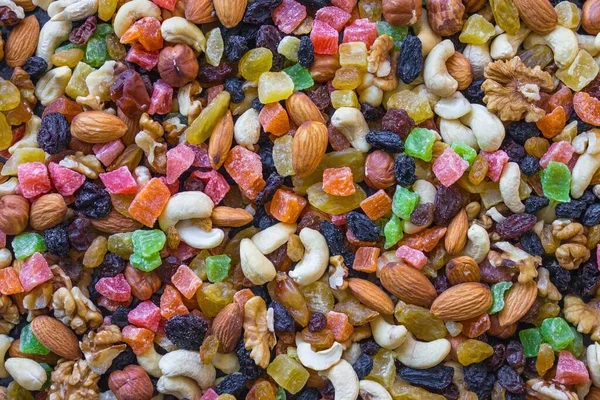 Nuts of different varieties are mixed with bright candied fruits. Nutritious mixture, delicious food, a source of vitamins and protein. View from above.