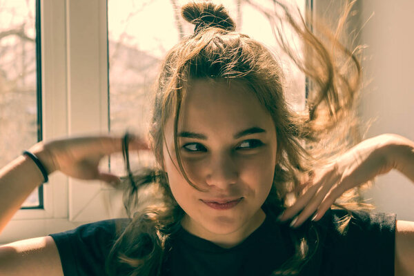 Девочка, подросток, школьница на фоне окна. Волосы трепещут, глаза смеются, довольная улыбка на лице. Беззаботность, счастье, радость
.