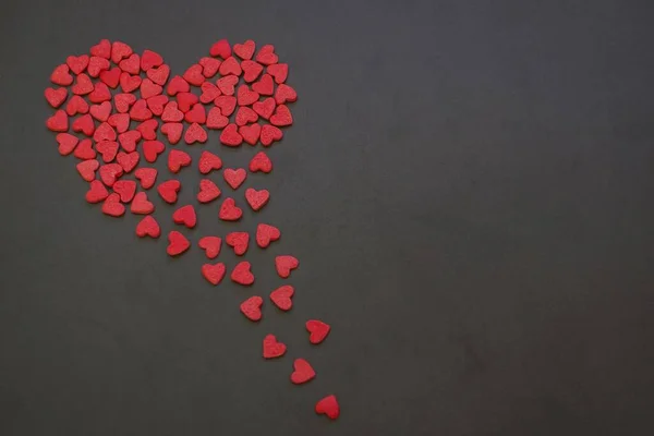 A large red heart consists of small hearts. It breaks into pieces, crumbles. Dark background, copy space.