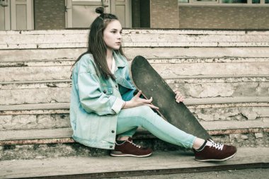 Eski basamaklarda kaykaylı genç bir kız. Modern gençlik, yeni nesil. Mavi kot ceket ve pantolon, spor ayakkabı. Uzağa bak. Sessiz ton, canlı ağ..