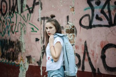Boyalı duvarın arkasındaki cesur kız. Uzun saçlı, meydan okumanın gözünde, protesto. Şehir tarzı, grunge, modern gençlik modası. Gündüz aydınlatma, canlı yayın.