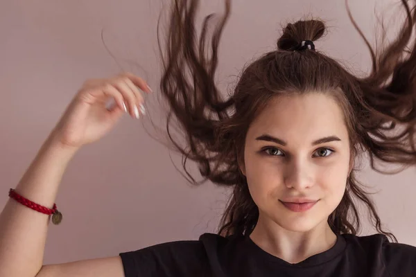 A young girl, a teenager, in a black T-shirt, with loose, flying hair. Straight look, easy smile. European appearance, green eyes. Light background, daylight.