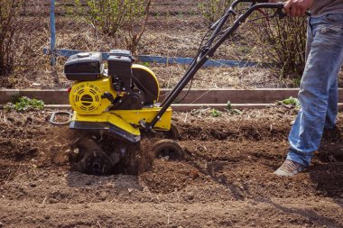 Bir adam sabanla bir bahçe sürüyor. Bahar, çiftlik, toprak. Arazi ekimi, bahçede bahar işi. Güneşli bir gün, doğal koşullar.