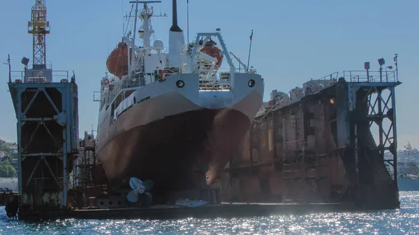 在一个特殊平台上的修理船坞里有一艘大船 附近是拆卸的船的螺丝 前面的景色阳光灿烂的日子 环绕着蓝色的大海 — 图库照片