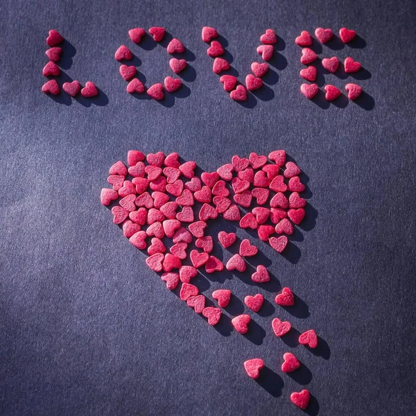 The word love and red heart on a dark background. Symbol of unhappy love, parting. The heart is made of small pieces. Side lighting, purple toning.