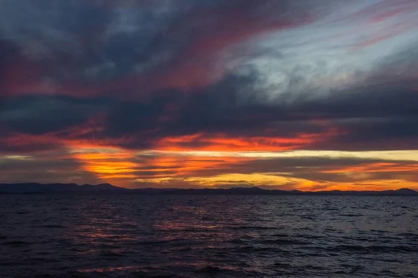 A dramatic, dark sky with storm clouds. Deep, rich colors. Around the sunset, the last rays of the sun. At sea there is a small ripple. Evening, natural lighting.