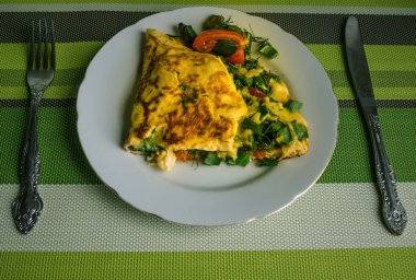 Beyaz tabakta omlet, bir tabak yumurta. Metal bıçak ve çatal, alt yeşil peçete. Geleneksel kahvaltı, ev yapımı yemek..