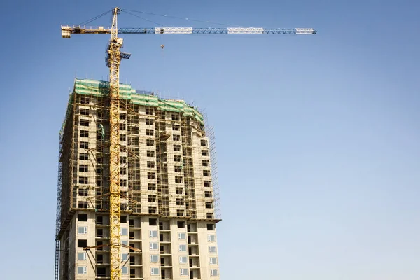 A tall building against the blue cloudless sky. Near the tower crane. Modern real estate, new building, shared construction. Bottom view, copy space.