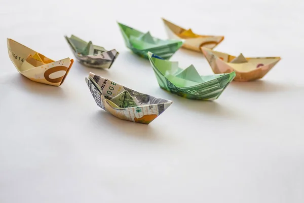 Two rows of paper ships made of euros and dollars. Prices for shipping, cruises. Light background,  copy space. The distant plan is blurred.