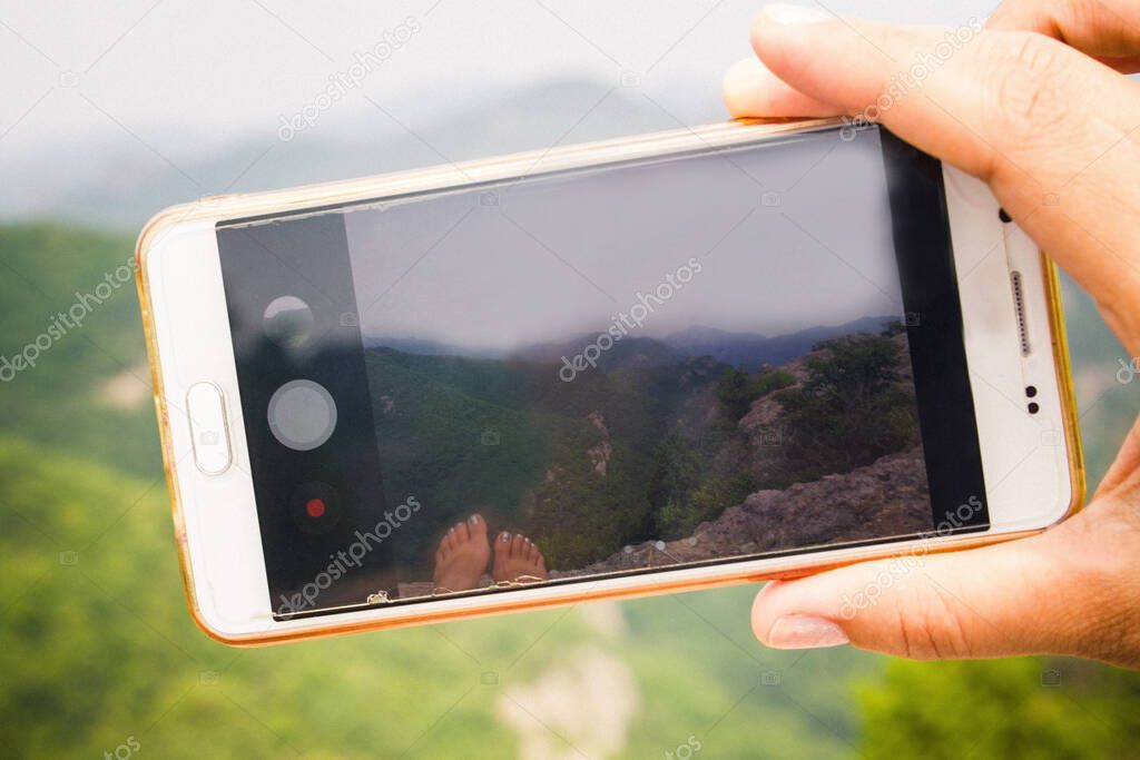 Hand with a smartphone. On the screen is a green landscape, mountains, sky, nature. Vacation, travel.