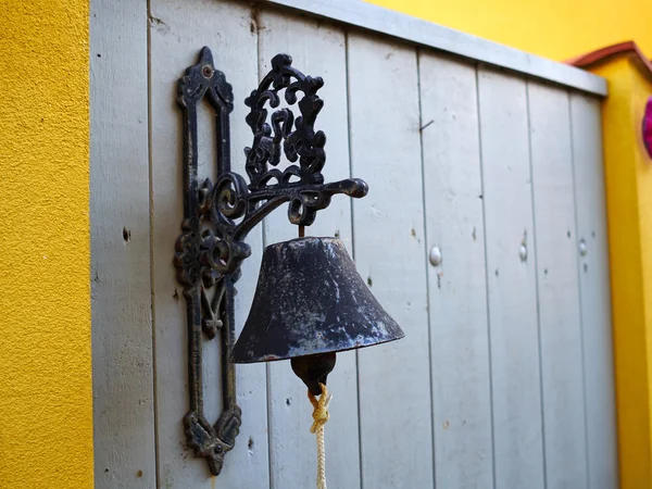 Old vintage metal bell hanging on a wooden fence door
