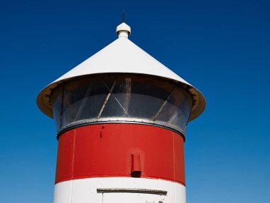 Deniz kıyısındaki küçük kırmızı ve beyaz deniz feneri güvenli bir yol göstericidir.