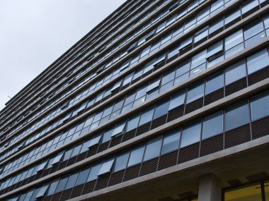 Sol üst köşesinde gri gökyüzü olan cam pencereli bir ofis binasının altından alçak açılı görüntü