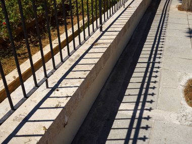 Demir çit ve gölgesi kaldırımda kaybolan bir bakış açısıyla kentsel arkaplan görüntüsü