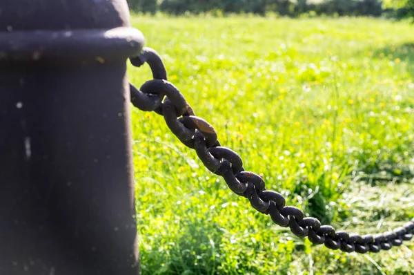 Säule mit Eisenkette auf Grashintergrund. Industrie, Natur. — Stockfoto