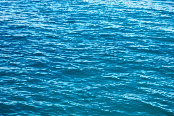 Heldere watertextuur in blauw. Achtergrond van de oceaan en de zee verlicht door de zon. — Stockfoto