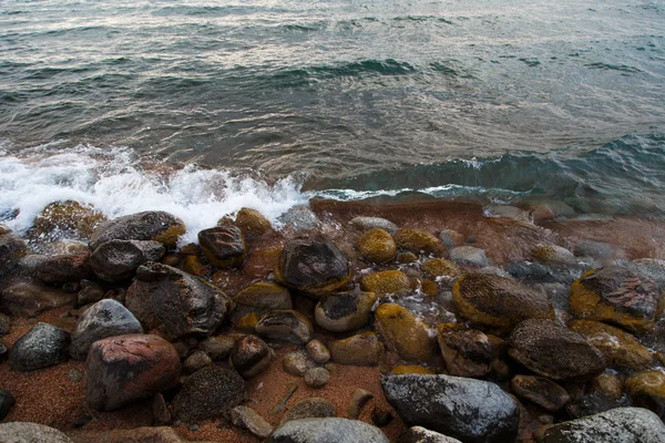 Piedras en la playa del mar. Día de invierno de pastos. Agua clara y arena. Kirguistán, lago Issyk-Kul — Foto de Stock