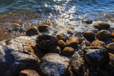 Stones on the sea beach. Pasture winter day. Clear water and sand. Kyrgyzstan, Issyk-Kul Lake