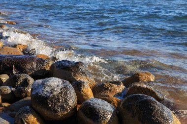 Stones on the sea beach. Pasture winter day. Clear water and sand. Kyrgyzstan, Issyk-Kul Lake