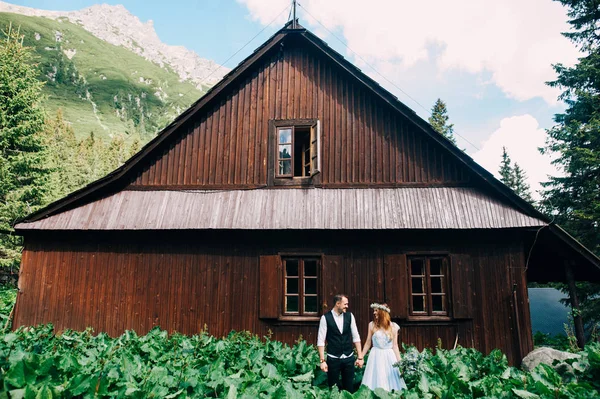 Жених и невеста, стоящие у деревянного дома в горах — стоковое фото
