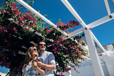 Genç bir çift örgülü çiçekli beyaz bir pergola altında duruyor