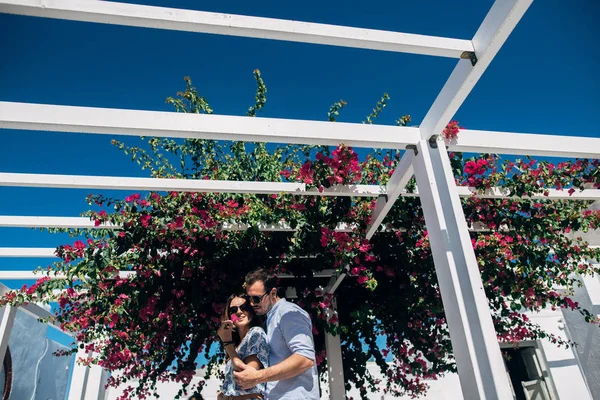 Una joven pareja está de pie bajo una pérgola blanca con flores trenzadas —  Fotos de Stock