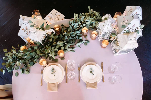 Wedding table for two decorated with white wooden candle lamps and flowers, fork and knife and glases beside plate