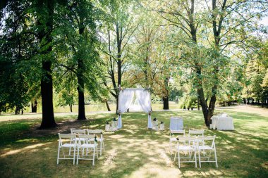 Açık havada düğün töreni, çiçeklerle süslenmiş sandalyeler ve kurdeleler çimlerin üzerinde sıra sıra durur.