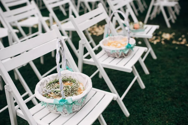 Outdoor wedding ceremony, chairs decorated withbasket with ros petals stand in rows on the grass — Stock Photo, Image