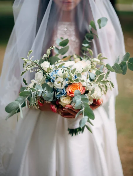 Bride holds wedding bouquet with peach roses and greens Royalty Free Stock Photos