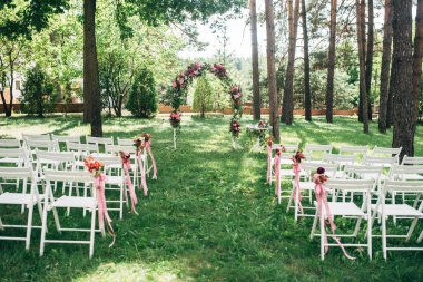Ormandaki düğün töreni. Kemer ve beyaz sandalye dekore edilmiş çiçekler ve şeritler