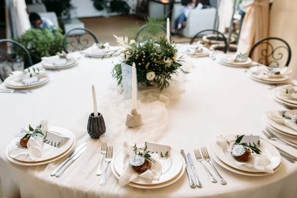 Украшенные столы с тарелками, ножами, вилками и букет с белыми цветами и зеленью по центру — стоковое фото