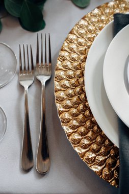 Tablo altın tabaklar, mumlar ve yeşillik üzerinde beyaz masa örtüsü ile dekore edilmiş