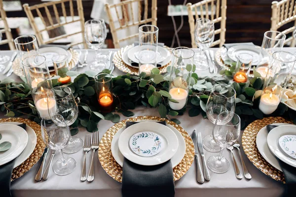 Dekorierter Tisch mit goldenen Tellern, Kerzen und Grüntönen auf der weißen Tischdecke — Stockfoto