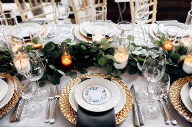 Tablo altın tabaklar, mumlar ve yeşillik üzerinde beyaz masa örtüsü ile dekore edilmiş