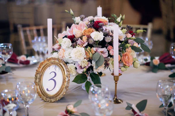 Mesas decoradas em ouro e cores borgonhas com placas, facas e garfos, velas e óculos, buquê com flores e verdes no centro — Fotografia de Stock