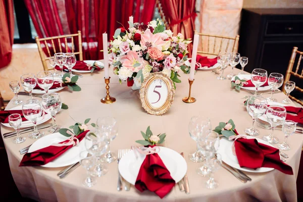 Mesas decoradas em ouro e cores borgonhas com placas, facas e garfos, velas e óculos, buquê com flores e verdes no centro — Fotografia de Stock