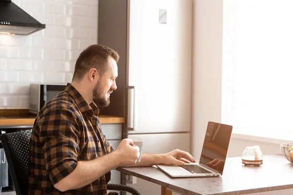 El tipo con una taza de café está trabajando en un portátil . — Foto de Stock