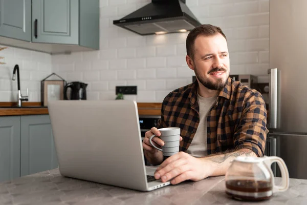 Typ mit einer Tasse Kaffee arbeitet an einem Laptop. — Stockfoto