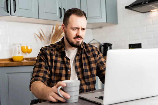 Kerel met een kop koffie werkt aan een laptop. — Stockfoto