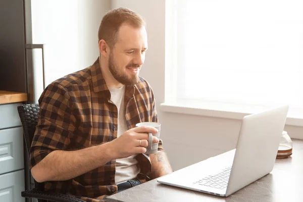 Kerel met een kop koffie werkt aan een laptop. — Stockfoto
