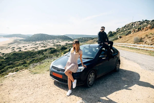 Couple sitting on a car, sea and mountain on background — 스톡 사진