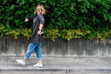 Kız turist elinde kamerayla yürüyor.