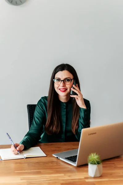 Mujer trabaja con un ordenador portátil y habla por teléfono —  Fotos de Stock