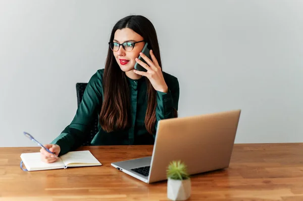 Mujer trabaja con un ordenador portátil y habla por teléfono —  Fotos de Stock