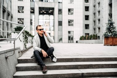 Attractive guy in casual coat sits on the steps