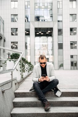 Attractive guy in casual coat sits on the steps
