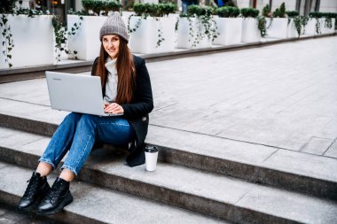 Dizüstü bilgisayarı olan bir kadın merdivenlerde oturuyor.